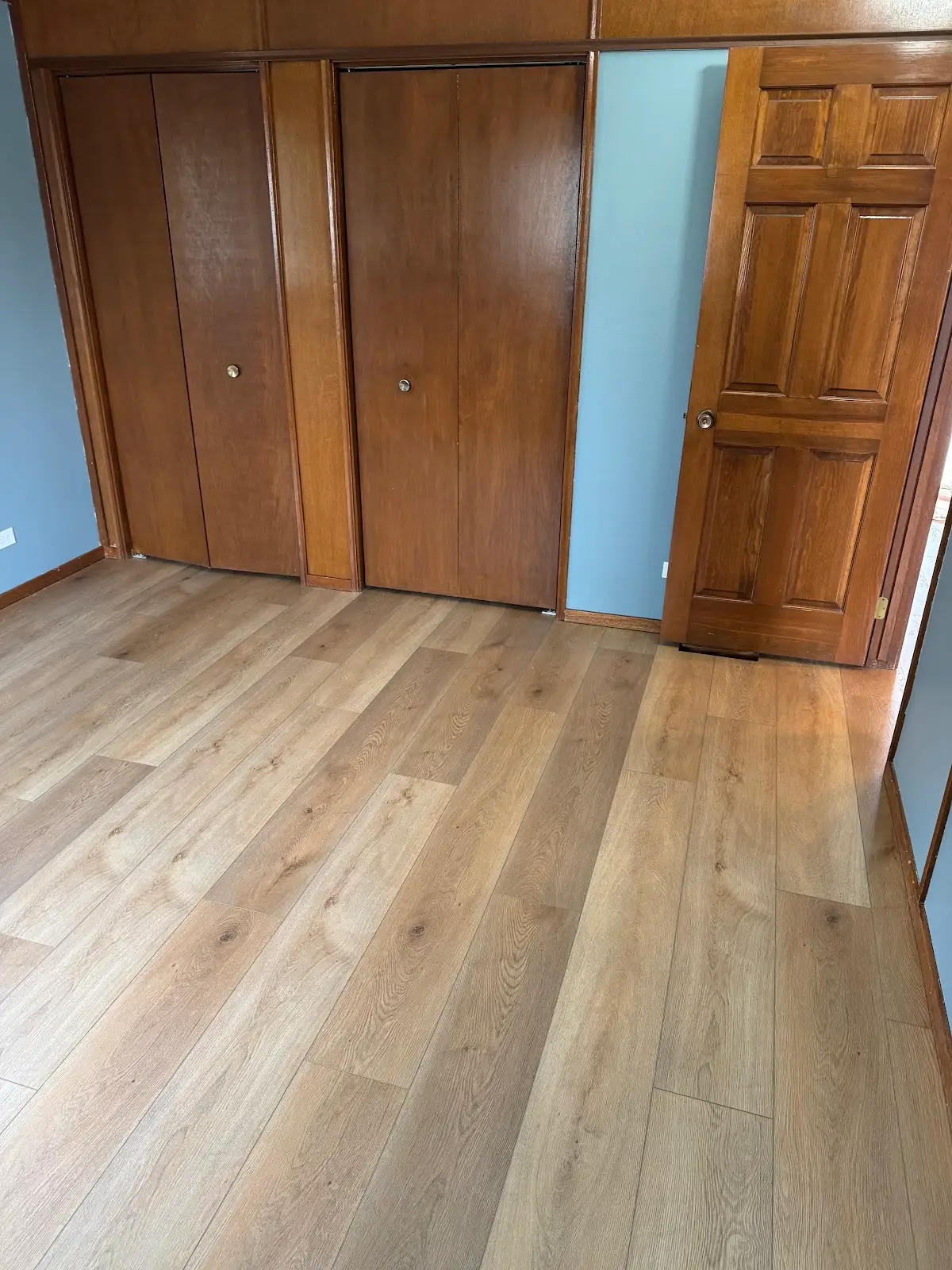 Wide-plank light oak luxury vinyl in a bedroom with wood closet doors